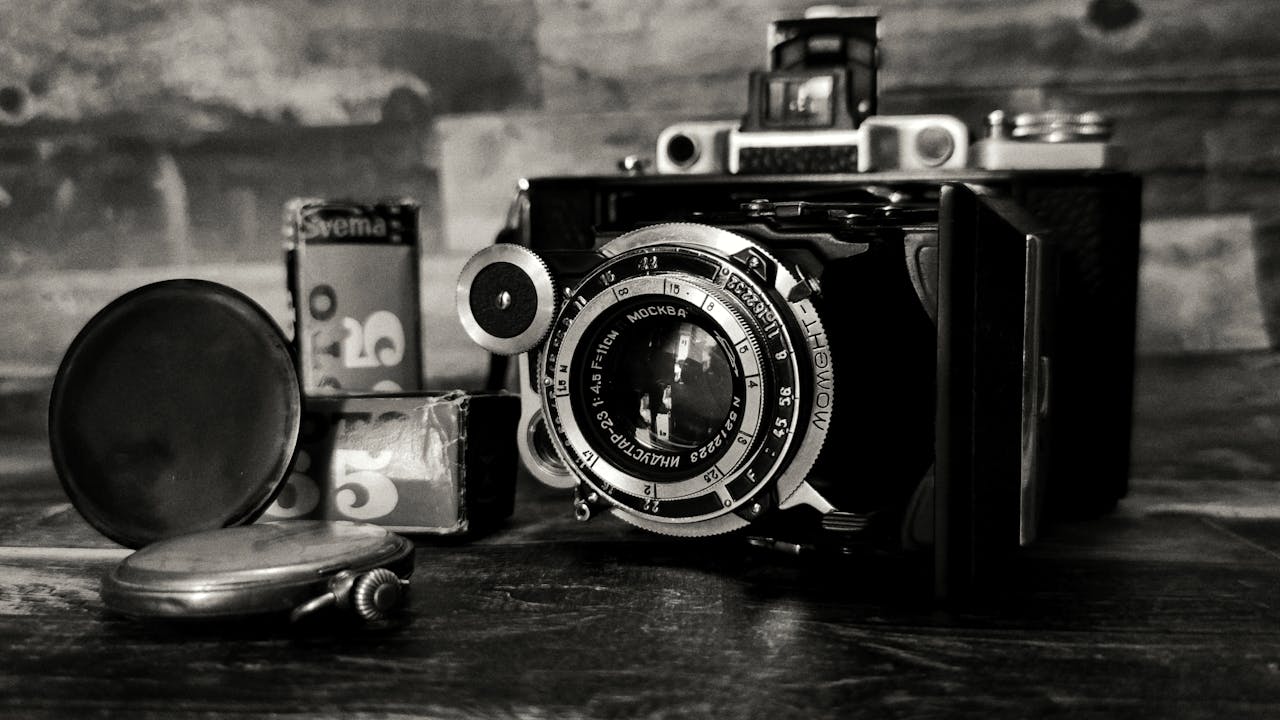 A black and white close-up of a vintage camera with film rolls, embodying retro charm.